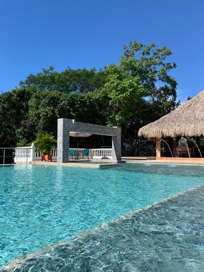 A clear swimming pool with a thatched-roof structure and a covered seating area. - Hotel Monte Bello (Doradal)