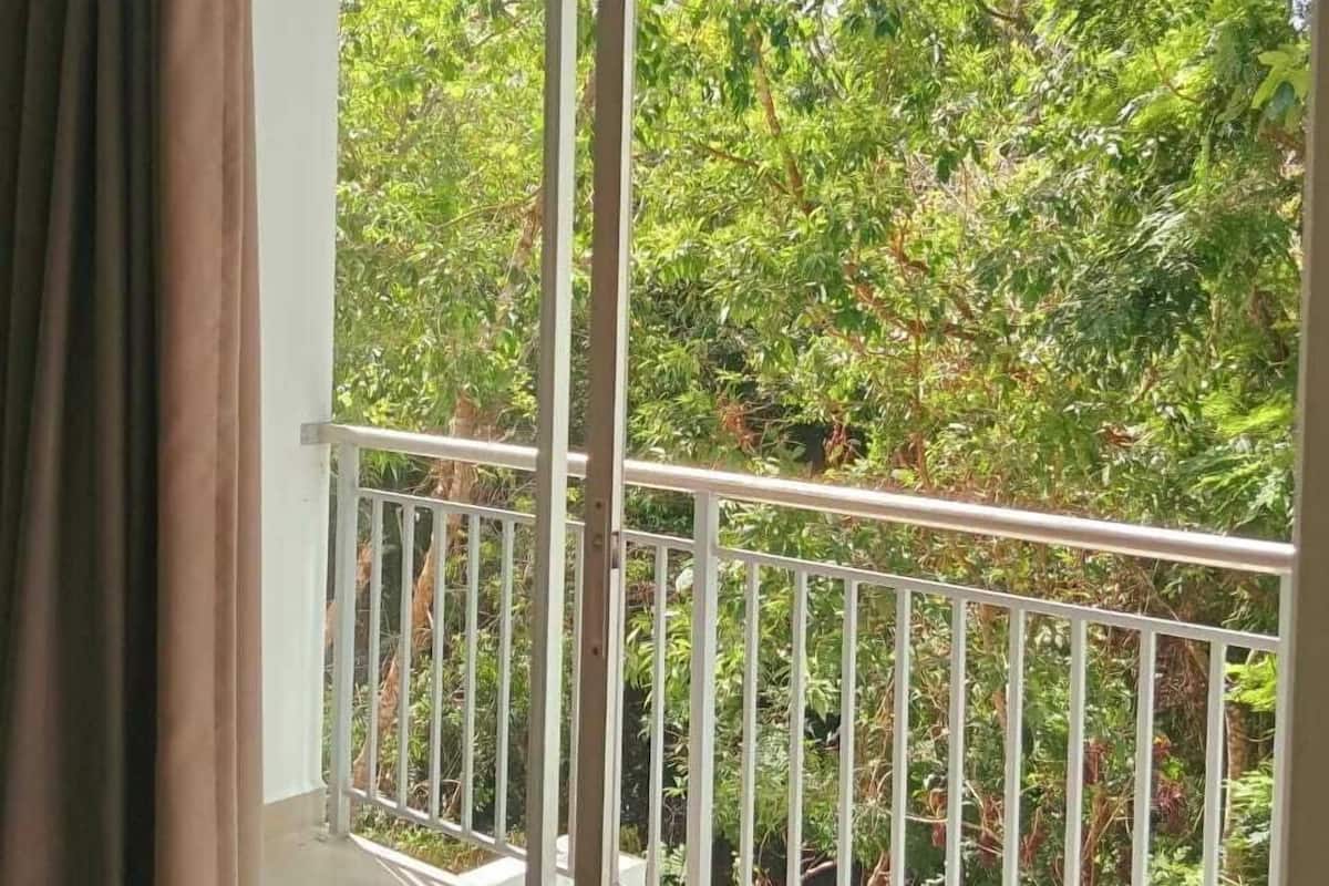 A balcony with a white railing, a sliding glass door, and a view of dense green foliage.