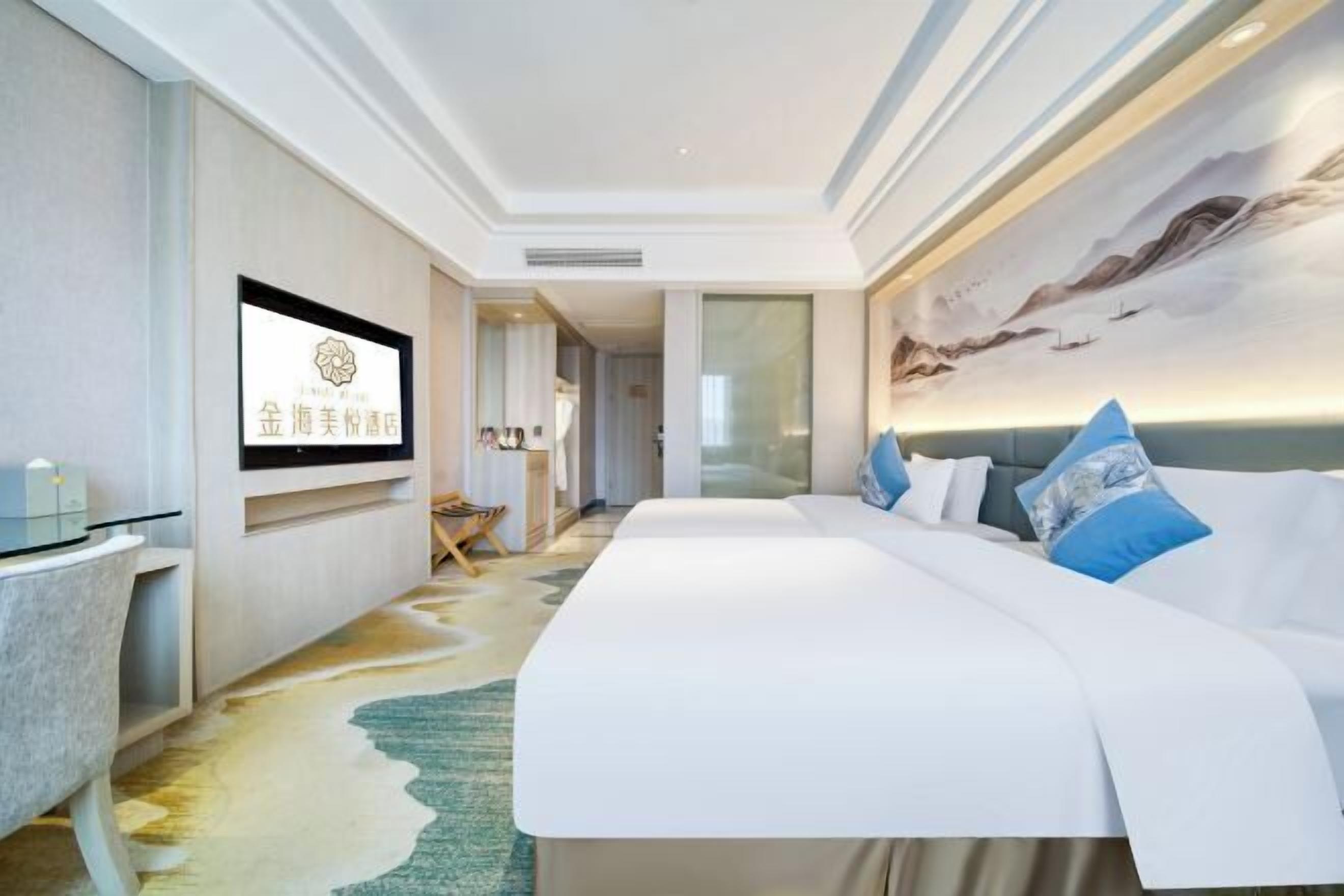 A hotel room with a large bed, a flat-screen TV mounted on the wall, a desk with a chair, and a decorative rug.