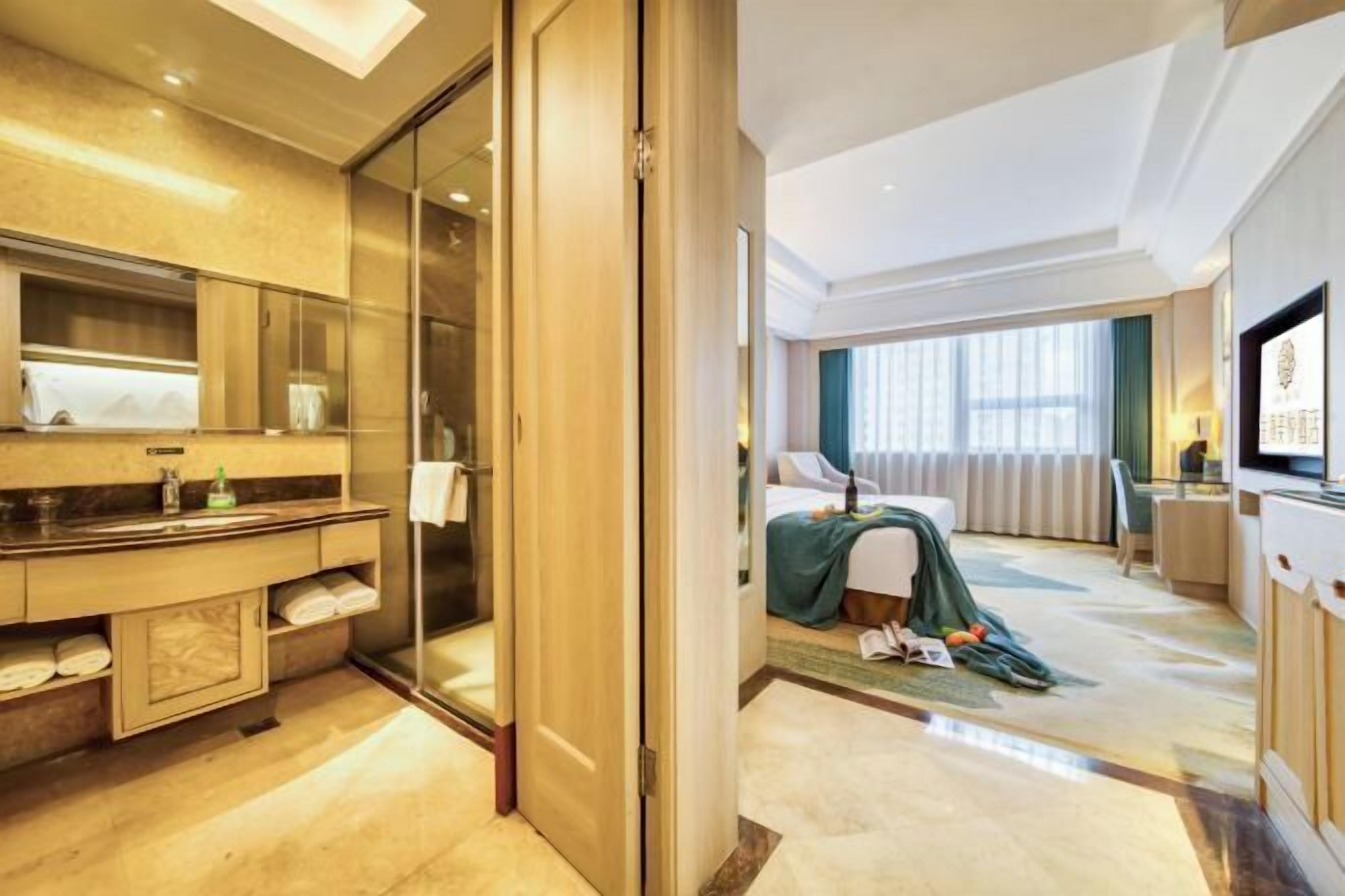 A hotel room with a bathroom, a bed, a desk, and a television.