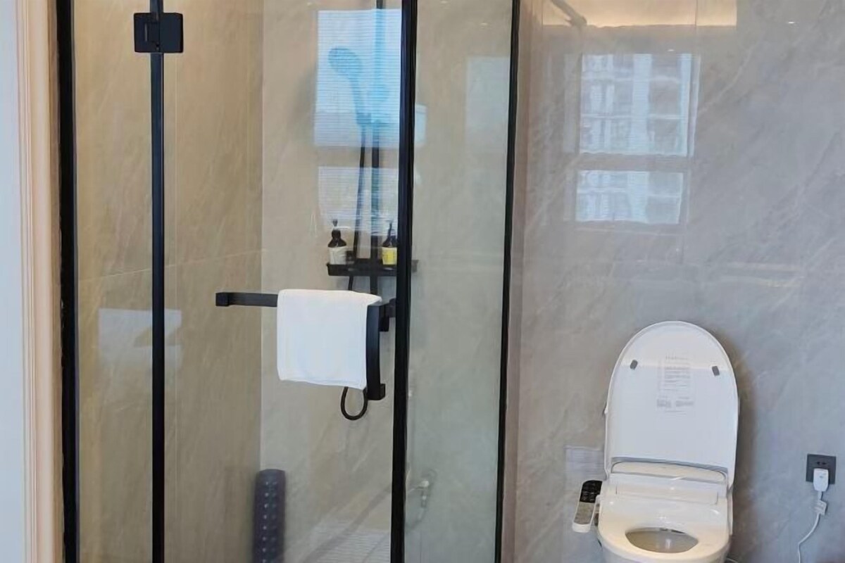 A modern bathroom with a glass shower enclosure, a toilet, and a hand dryer.