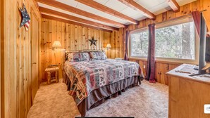A wooden cabin bedroom with a bed, two lamps, a star decoration, and a window with curtains. - Charming 2-bedroom house in Ruidoso with AC, WiFI, pellet stove, hot tub (Ruidoso)