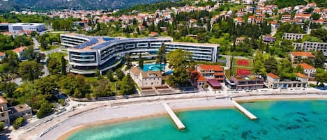 A coastal hotel with a pool, surrounded by residential buildings and mountains.