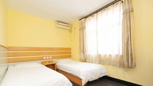 A room with two beds, a wooden headboard, a small bedside table, and a window with curtains.