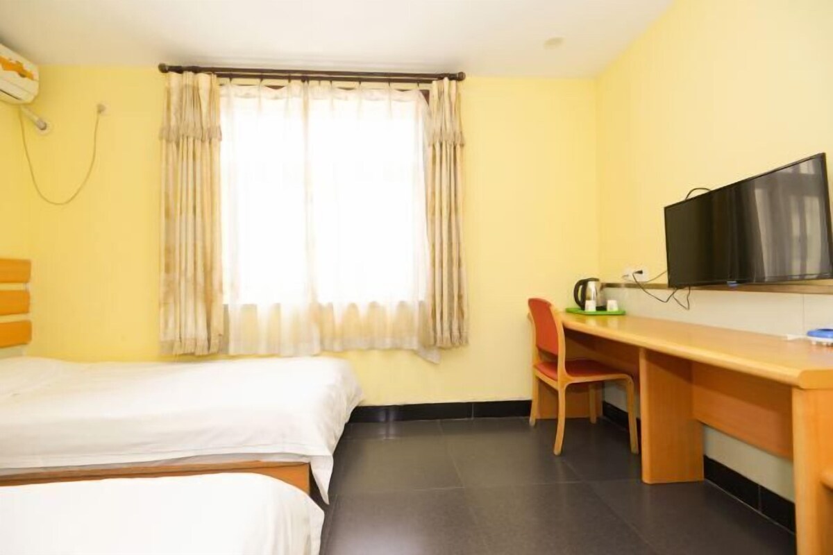A hotel room with two beds, a desk, a chair, a television, and a window with curtains.