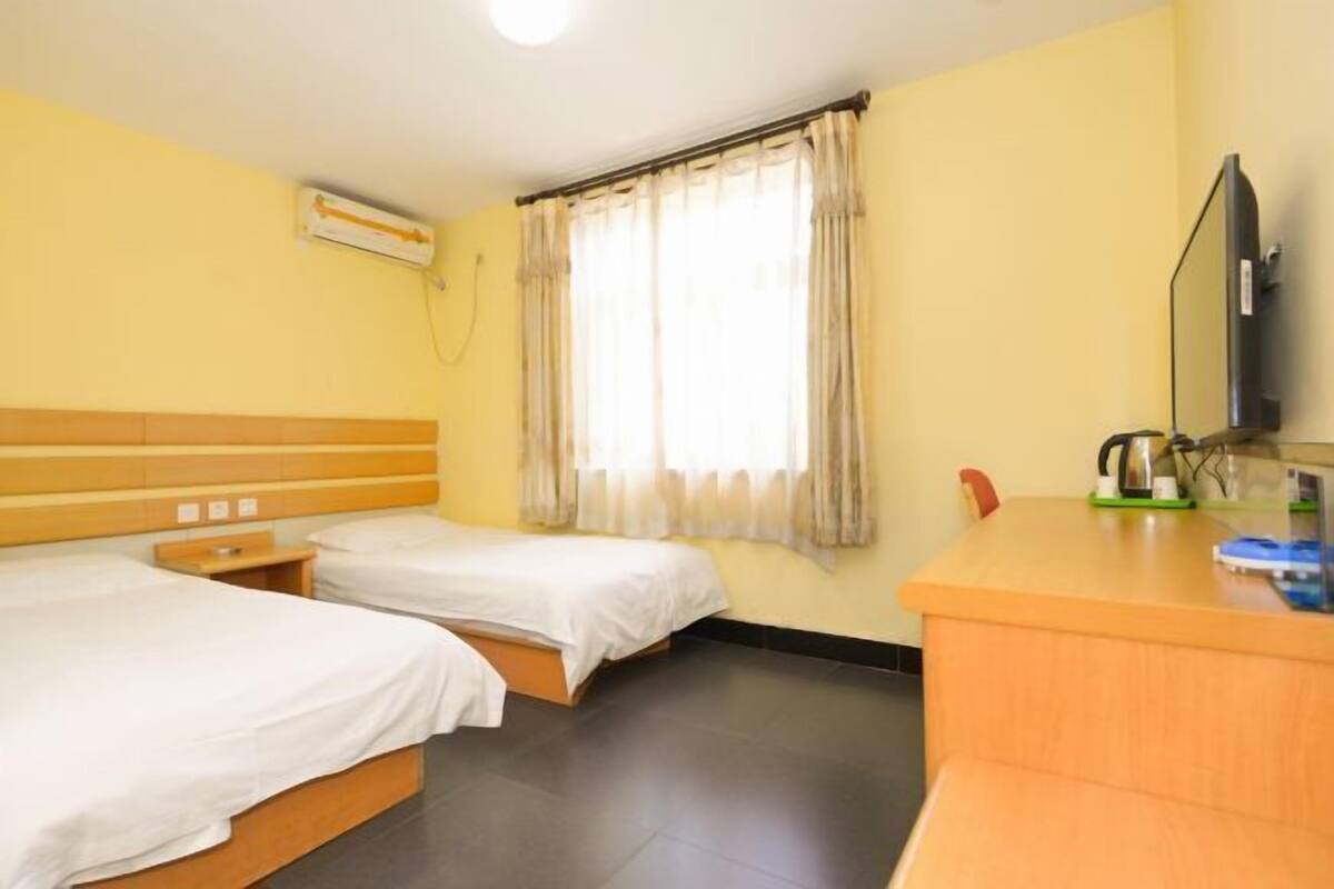 A hotel room with two beds, a wooden headboard, a desk with a kettle, and a television.