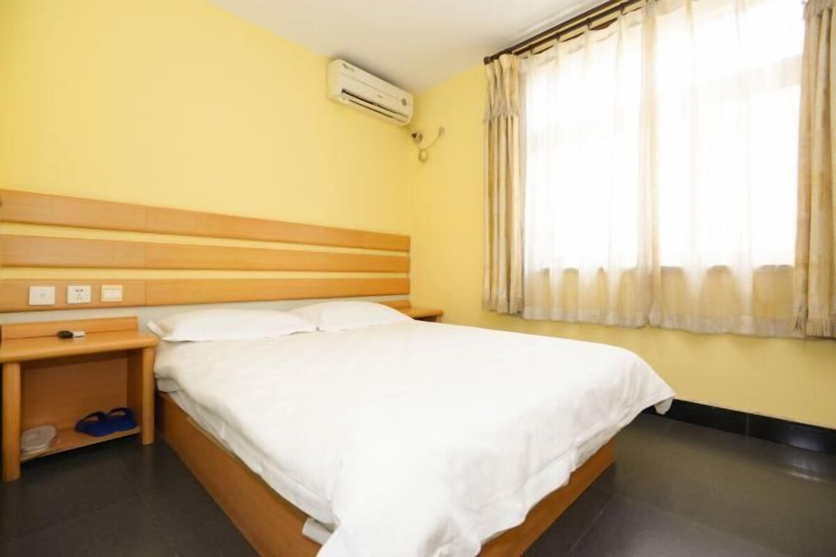 A single bed with a wooden headboard, a bedside table, and an air conditioning unit on the wall.