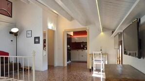 Amplia sala de estar con una cocina al fondo, una mesa de comedor con sillas y un televisor montado en la pared.