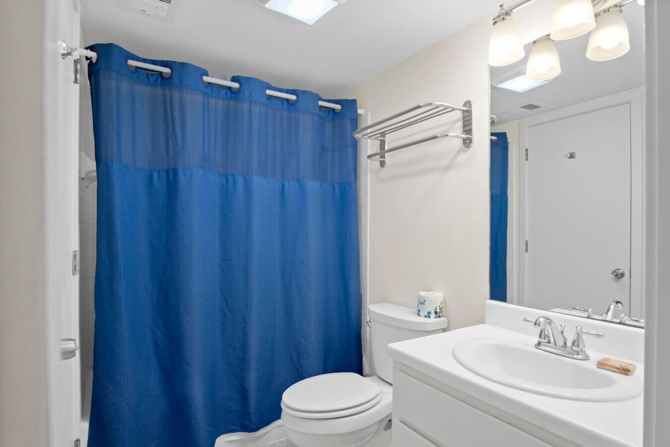 Un baño con inodoro blanco, lavamanos con espejo y cortina de ducha azul.