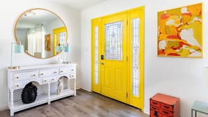 A bright yellow door with a decorative glass panel, a white console table with drawers, and a large round mirror. - Mid-Century Modern | Pool & Spa | Mountain Views (Palm Springs)