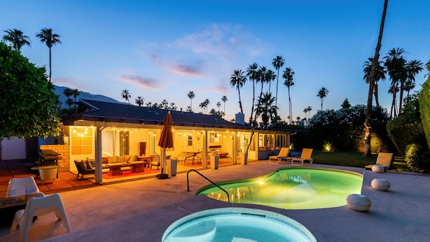 A pool area with a hot tub, lounge chairs, and a covered patio with string lights. - Mid-Century Modern | Pool & Spa | Mountain Views (Palm Springs)