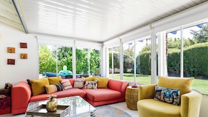 A spacious living room with a red sectional sofa, a yellow armchair, and a glass coffee table. Large windows provide a view of the garden. - Mid-Century Modern | Pool & Spa | Mountain Views (Palm Springs)