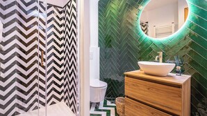 A modern bathroom with a zigzag patterned shower enclosure, a round mirror with green lighting, and a wooden vanity with a white sink. - Patio Suite - Unique and Close to the Sea in El Campello (El Campello)