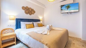 Ein Hotelzimmer mit Bett, Wandfernseher, Wanddeko und einem Korbstuhl.