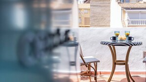 Een balkon met een tafel voor twee personen, voorzien van een glazen blad en twee bekers sap.