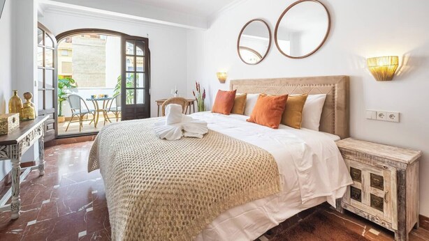 Un dormitorio bien iluminado con una cama grande, dos espejos en la pared y vistas al balcón exterior.
