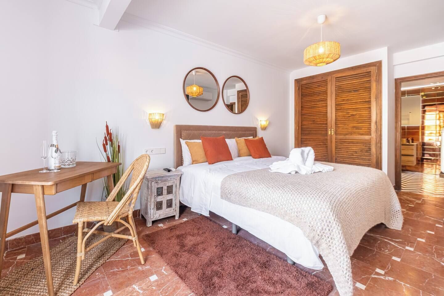 A hotel room with a bed, a wooden desk, a chair, a nightstand, and a mirror.