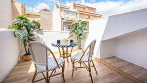 Un pequeño patio al aire libre con sillas de mimbre y una mesa redonda, rodeado de plantas en macetas.