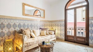 Una habitación con pared de baldosas con diseño, un sofá color beige con cojines, una pequeña mesita de madera y un amplio arco de entrada.