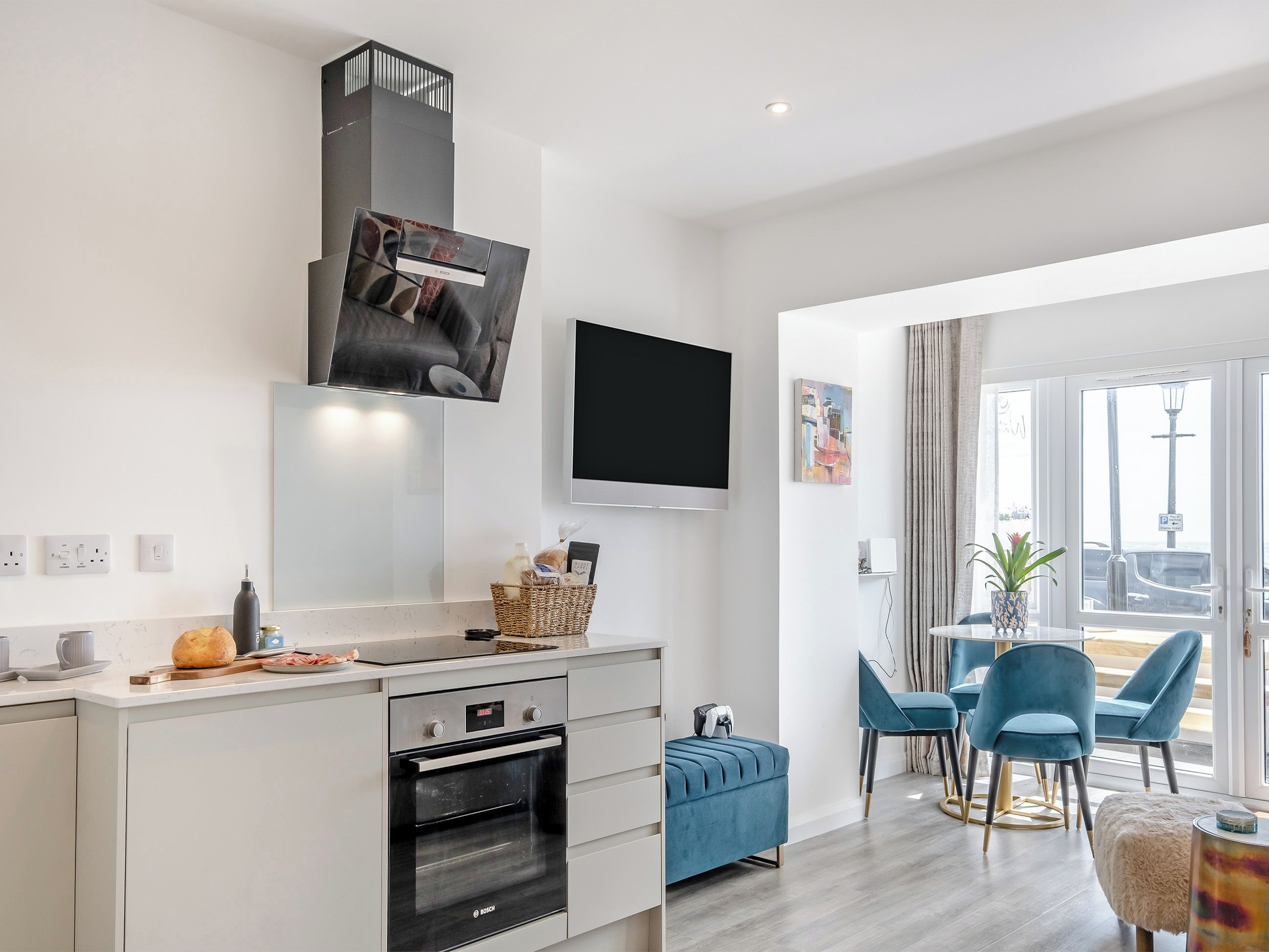 A modern kitchen with a Bosch oven, a dining area with blue chairs, and a large window with a view.