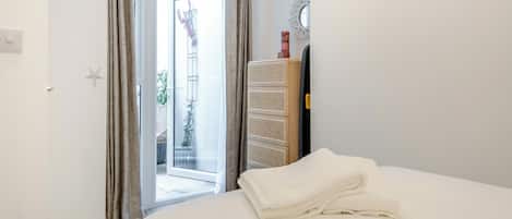 Een slaapkamer met een bed, een kledingkast, een deur die leidt naar een balkon en een wandlamp.