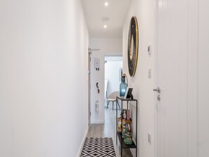 Un couloir avec un tapis à motifs, une étagère contenant divers objets et un élément décoratif fixé au mur.