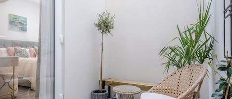 Ein kleiner Balkon mit Korbstuhl, Topfpflanze und Glastür zum Schlafzimmer.