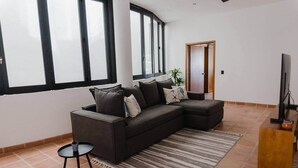 Ein modernes Wohnzimmer mit einem Ecksofa, einem kleinen Beistelltisch, einem Fernseher und einem großen Fenster.
