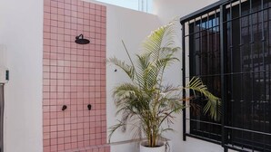 Ein Gebäudeeck mit einer rosa gefliesten Wand, einem schwarzen Metallfenster und einem Blumentopf.