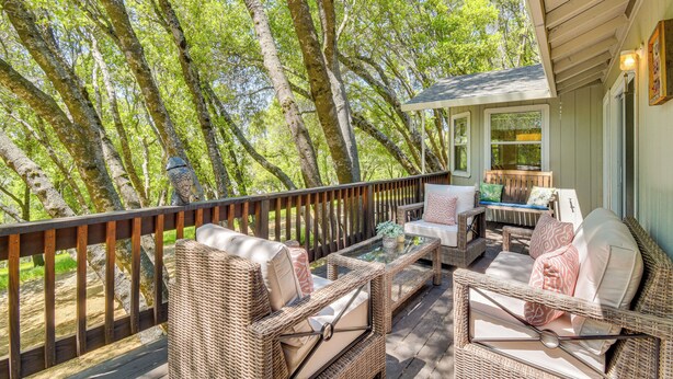 A covered outdoor seating area with wicker furniture and a glass table, surrounded by trees. - Yosemite Home Base: Community Perks + Lake Access! (Groveland)