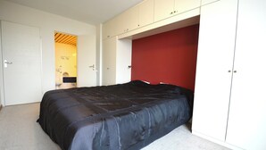 A bedroom with a bed, wardrobe, and a red accent wall. - Bright 3-bedroom Apartment With Sea View (Knokke-Heist)