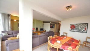 A living room with a sofa, a dining table with chairs, and a kitchen area in the background. - Bright 3-bedroom Apartment With Sea View (Knokke-Heist)