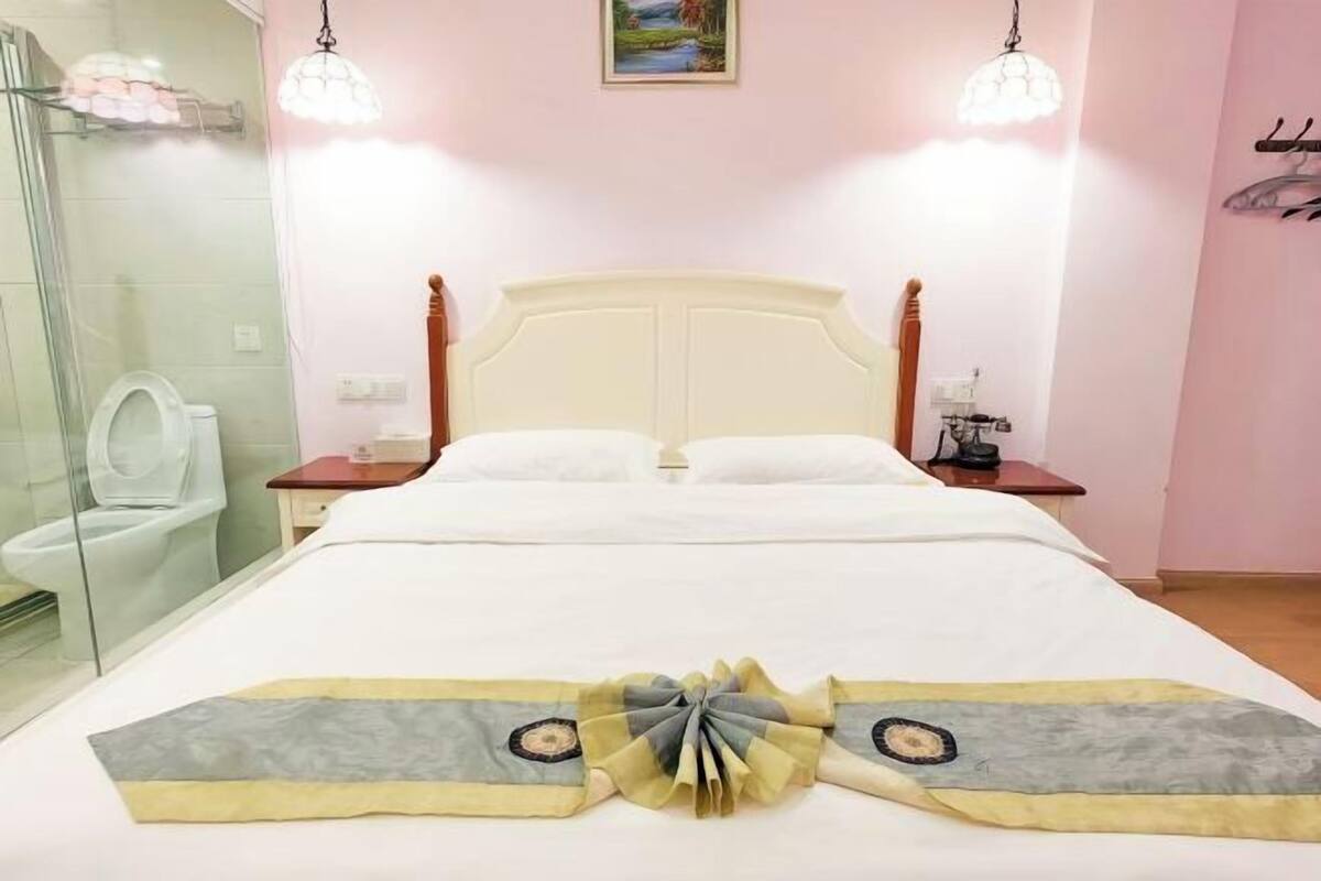 Ein Hotelzimmer mit Bett, Nachttisch, einem Bild an der Wand und einem Badezimmer mit Toilette und Dusche.