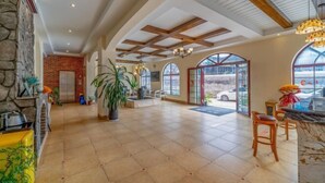 A spacious lobby with a stone wall, a fireplace, and a large potted plant. There are wooden beams on the ceiling and large windows with arched tops. - Mengzi Fengjing Boutique Hotel (Mengzi)