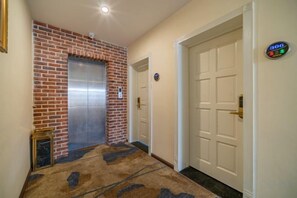 A hallway with a brick wall, an elevator, and a white door. - Mengzi Fengjing Boutique Hotel (Mengzi)