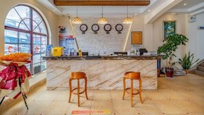 A hotel lobby with a marble reception desk, wooden stools, a large window, and a plant. - Mengzi Fengjing Boutique Hotel (Mengzi)