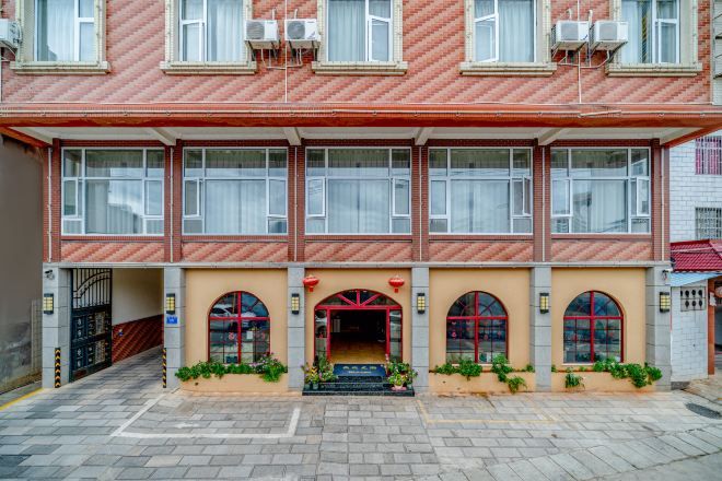 A two-story building with a red and beige facade, multiple windows, and a central entrance with a red archway.