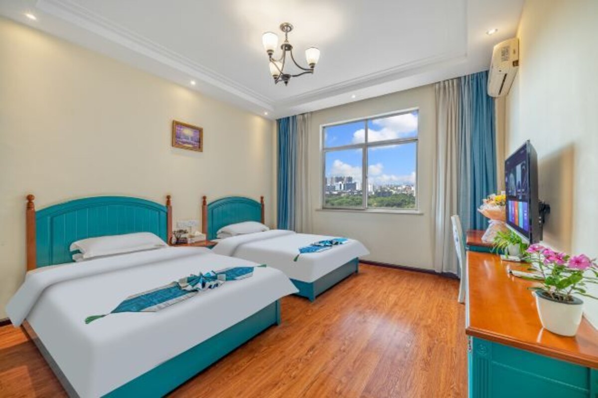 A hotel room with two beds, a TV, a desk with a plant, and a window with a city view.