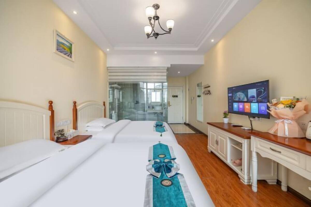 Ein Hotelzimmer mit zwei Betten, einem Fernseher, einem Schreibtisch und einem durch eine Glastür einsehbaren Badezimmer.