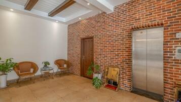 A lobby with a brick wall, an elevator, and seating area with chairs and tables.
