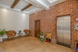 Un hall d’entrée avec un mur en briques, un ascenseur et un espace détente comprenant des chaises et des tables.