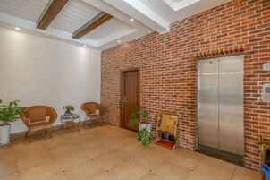 Un vestíbulo con pared de ladrillo, un ascensor y una zona de estar con sillas y mesas.