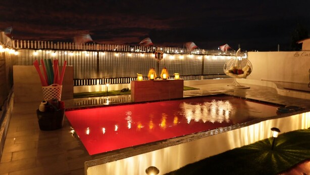 A rooftop terrace with a red pool, string lights, and a hanging chair.