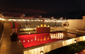 Une terrasse sur le toit avec une piscine rouge, des guirlandes lumineuses et un fauteuil suspendu.