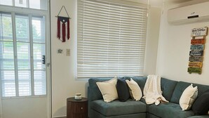 A living room with a sectional sofa, a ceiling fan, a window with blinds, a door, and a small side table.