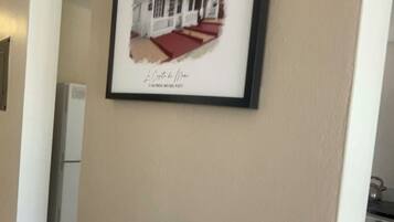 A framed picture of a house on a beige wall in a hallway.