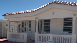 A white building with a tiled roof, a gated entrance, and a paved driveway.
