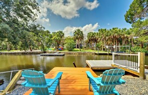 A wooden dock with two blue Adirondack chairs facing a calm lake, surrounded by lush greenery and palm trees. - Outdoor Oasis: Canal-Front Home in Crystal River (Crystal River)