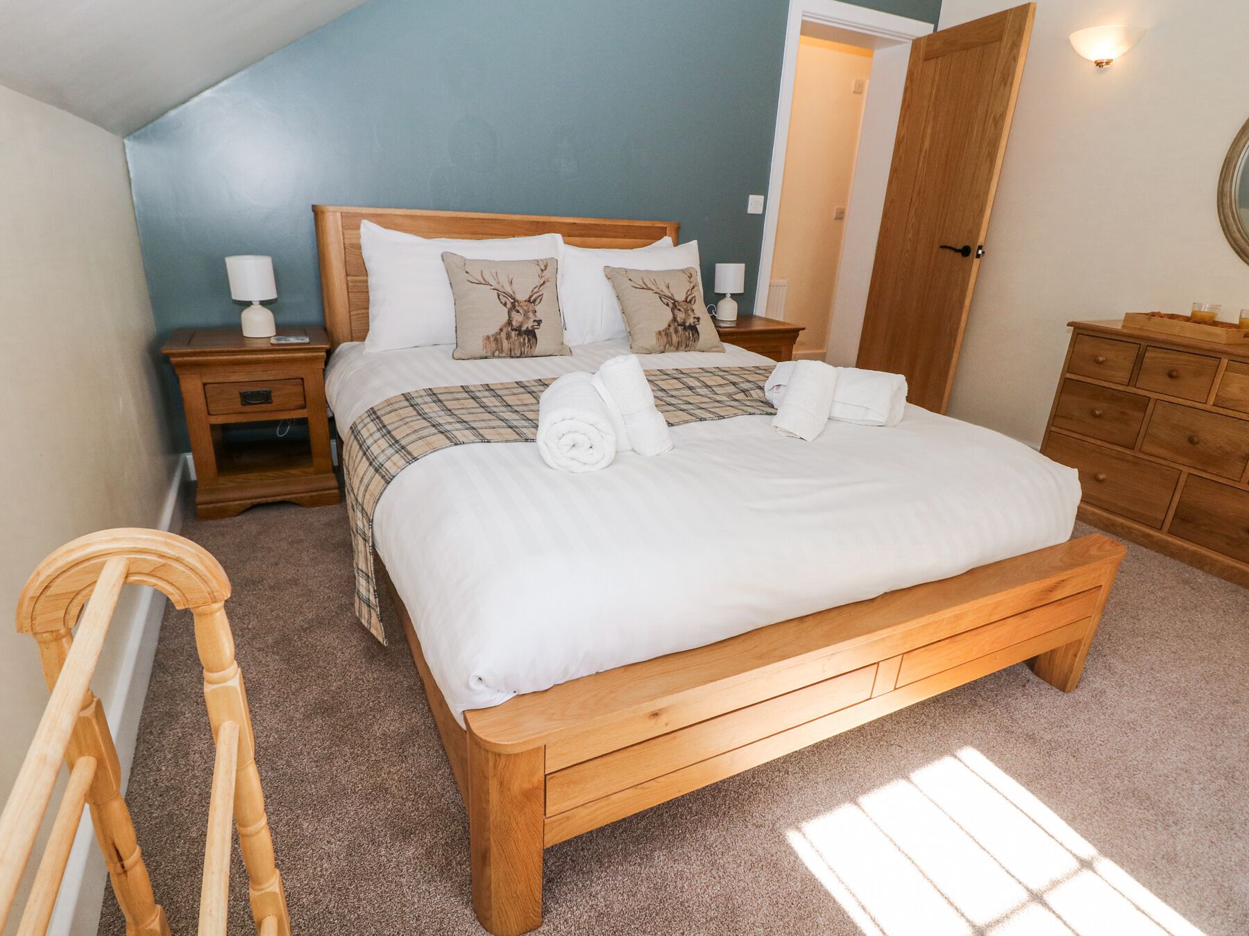 Un lit bien fait, avec du linge de lit blanc et deux oreillers, une table de chevet en bois avec une lampe, une commode en bois et une chaise en bois.