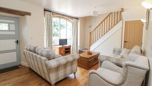 Ein Wohnzimmer mit Holzboden, zwei Sofas, einem Couchtisch aus Holz, einem Fernseher auf einem Schrank und einer Treppe.